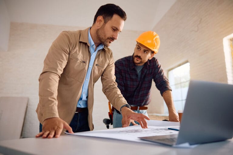 Two men discussing building plans on a table.